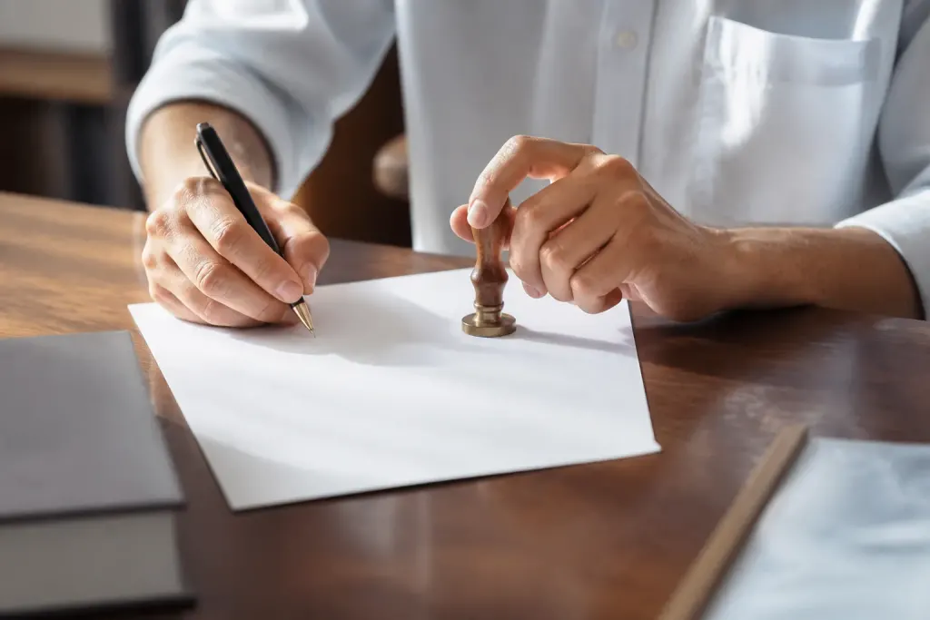 Mains signant document officiel avec tampon notarial visible